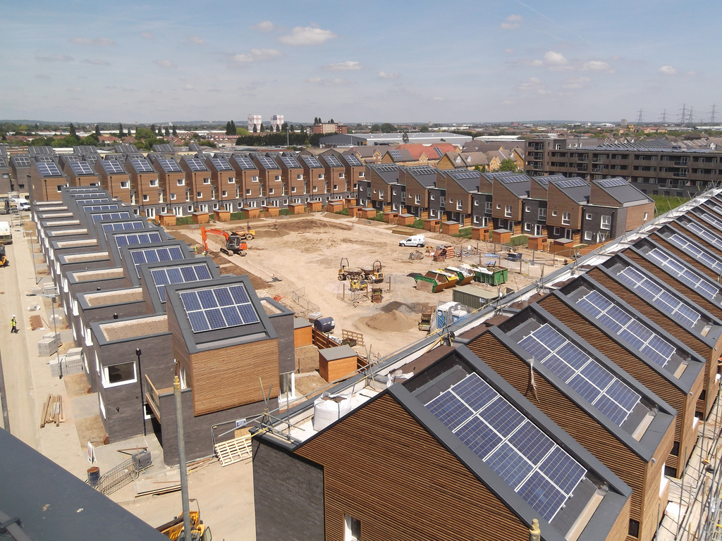 An overhead shot of a building site in progress. New houses are arranged in a square formation. There are solar panels on each roof. 
