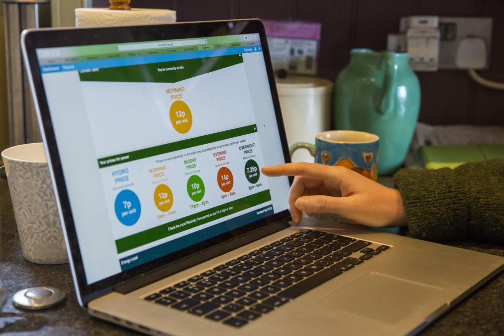 A hand points to an open laptop screen displaying Energy Local's energy dashboard. 