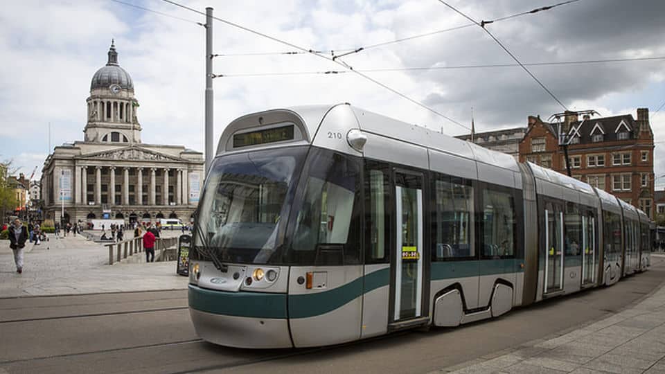 A silver and green tram passes by Nottingham's council house building. 