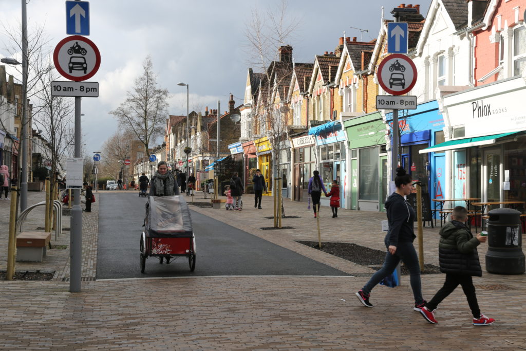 People walk down a high street with colourful shop fronts and good pedestrian access in Waltham Forest.