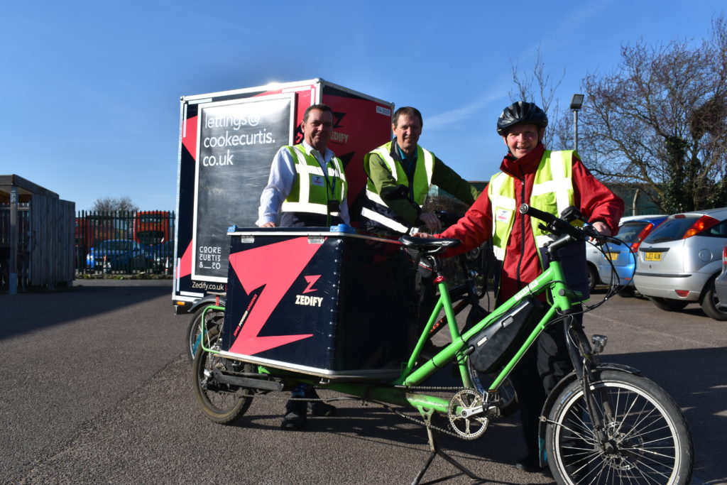 Three Zedify couriers in yellow hi-vis jackets pose with an e-cargo bike.